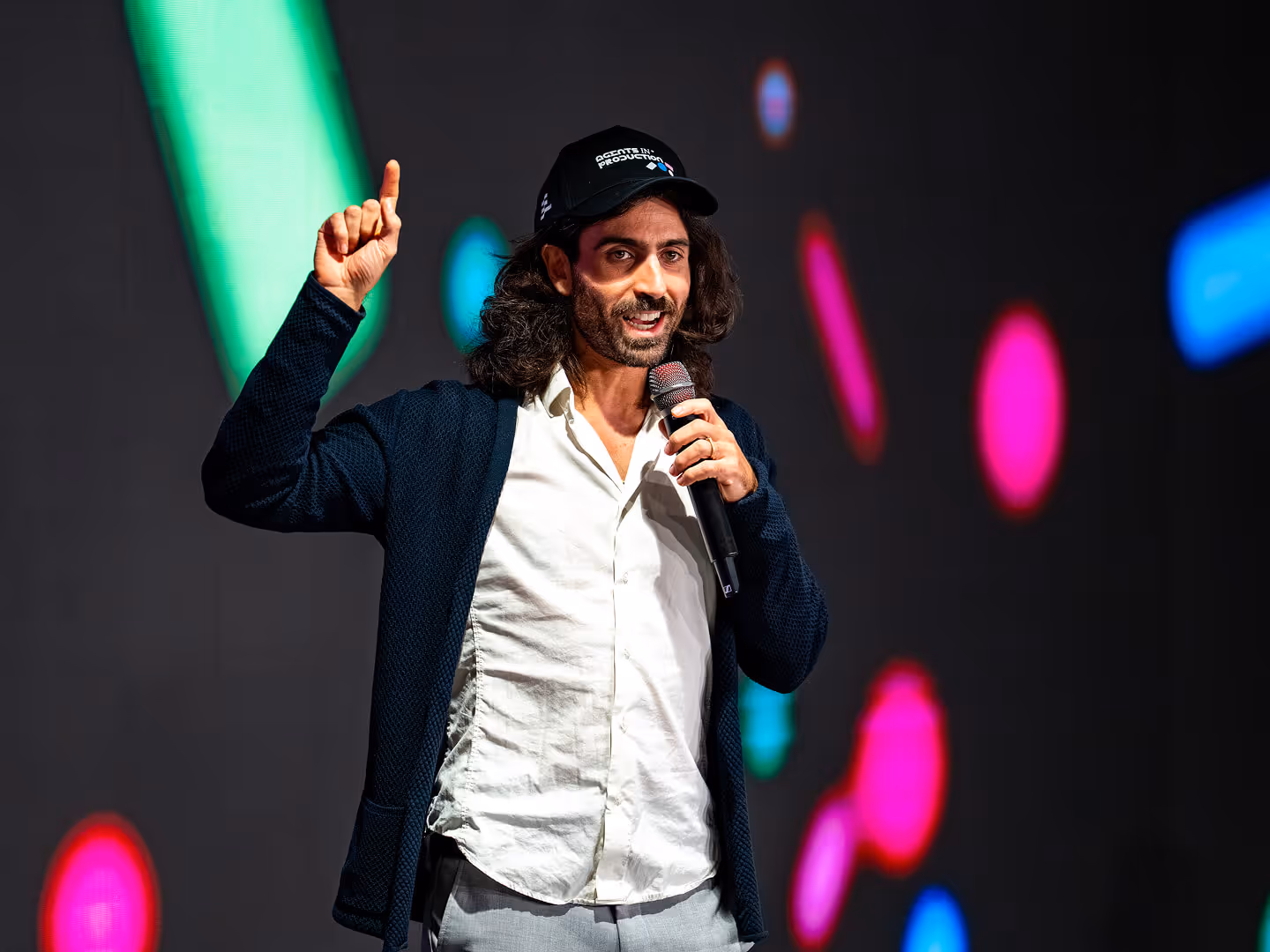 MLOps conference speaker holding a microphone and gesturing on a colorful stage
