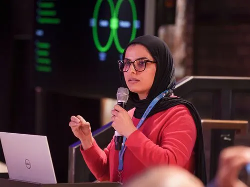 MLOps speaker in a headscarf presenting with a microphone beside a laptop and projected diagram