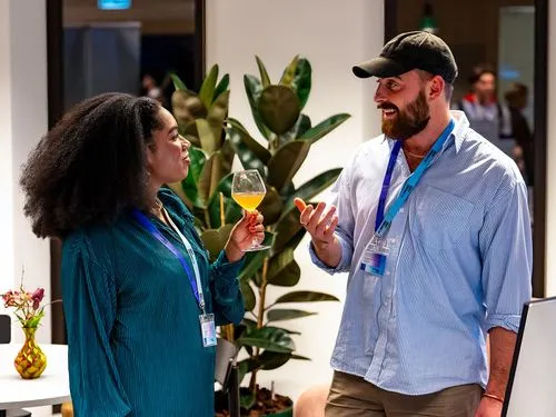 Two MLOps professionals networking at an event, chatting over drinks near indoor plants