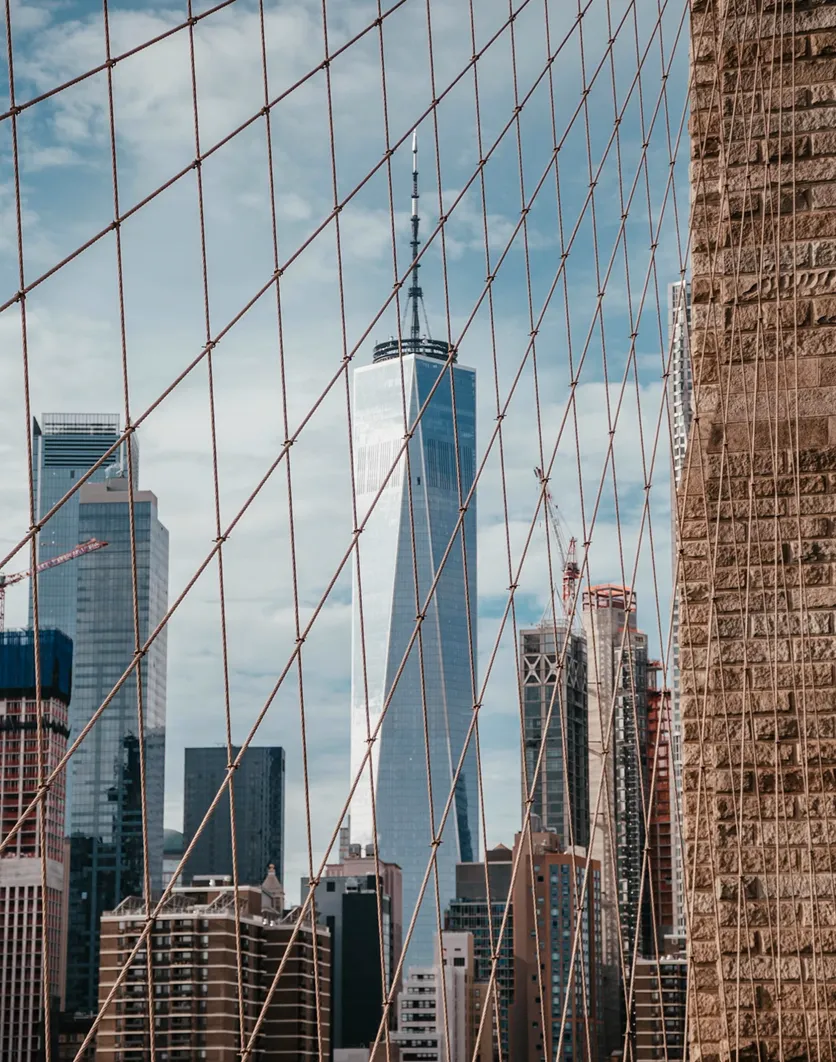 View of One World Trade Center and surrounding skyscrapers through the suspension cables of the Brooklyn Bridge.