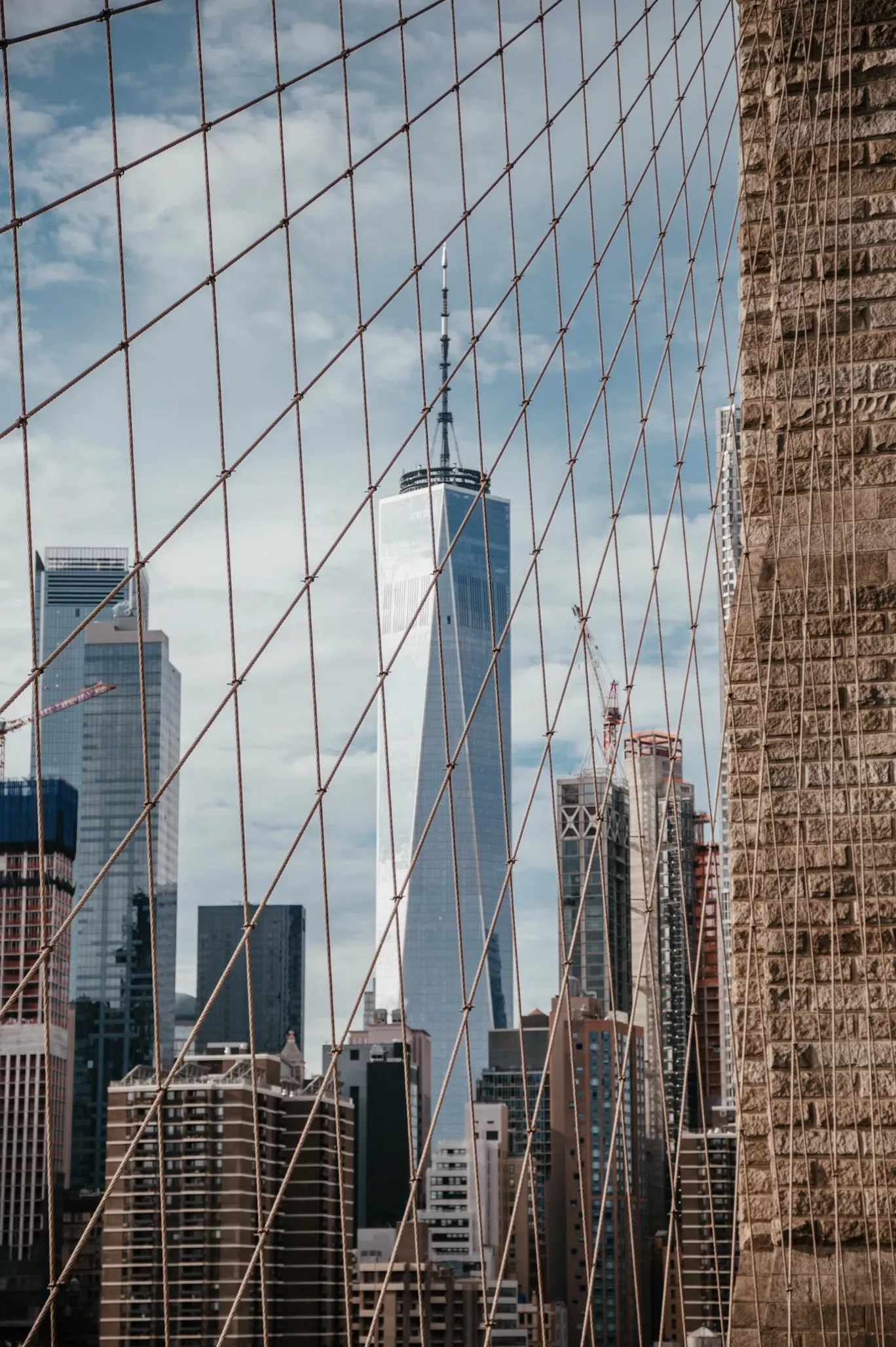 View of One World Trade Center and surrounding skyscrapers in New York City seen through the cables of the Brooklyn Bridge.