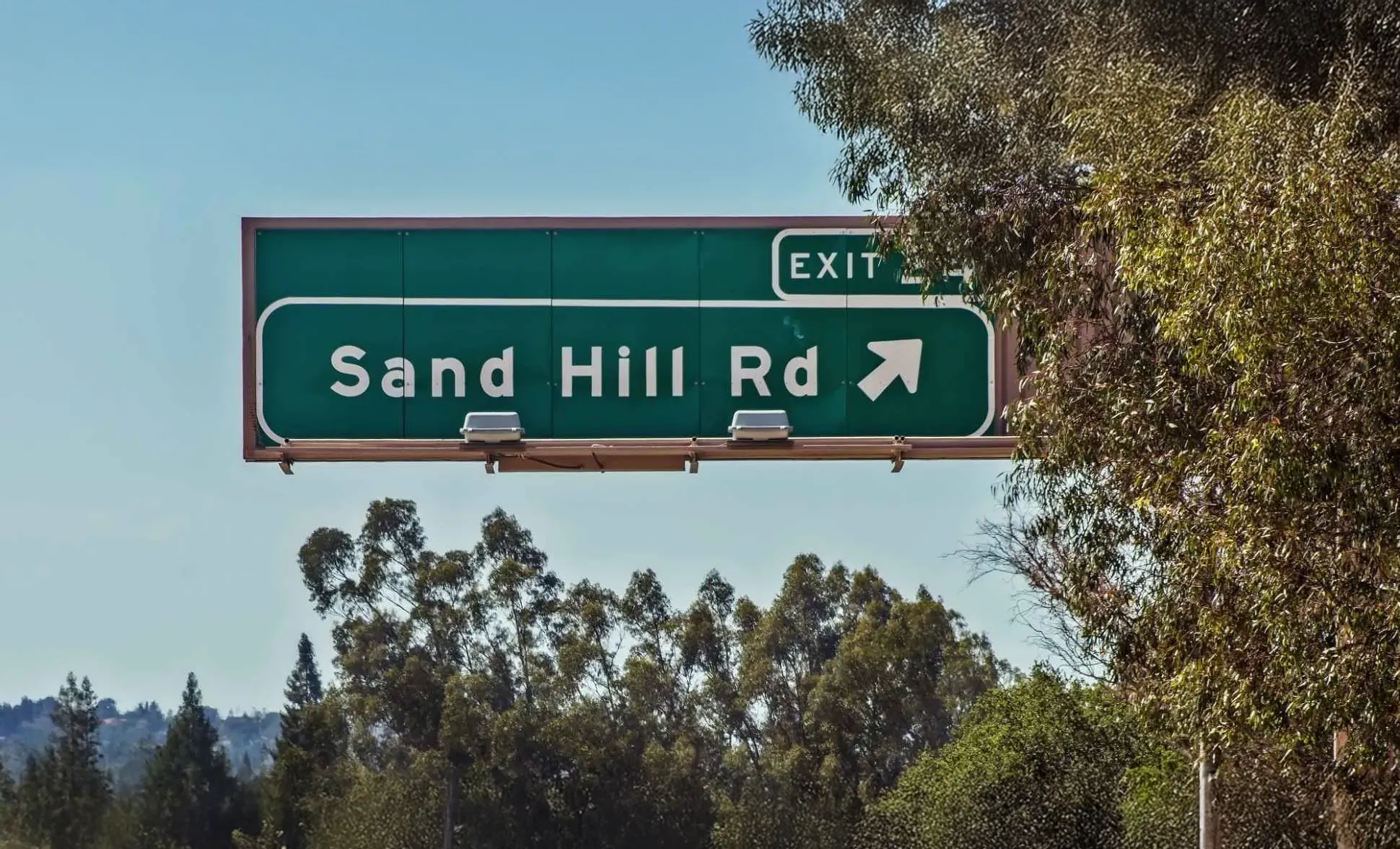 Vineyard rows in foreground with a distant town and rolling hills under a clear sky at sunset.