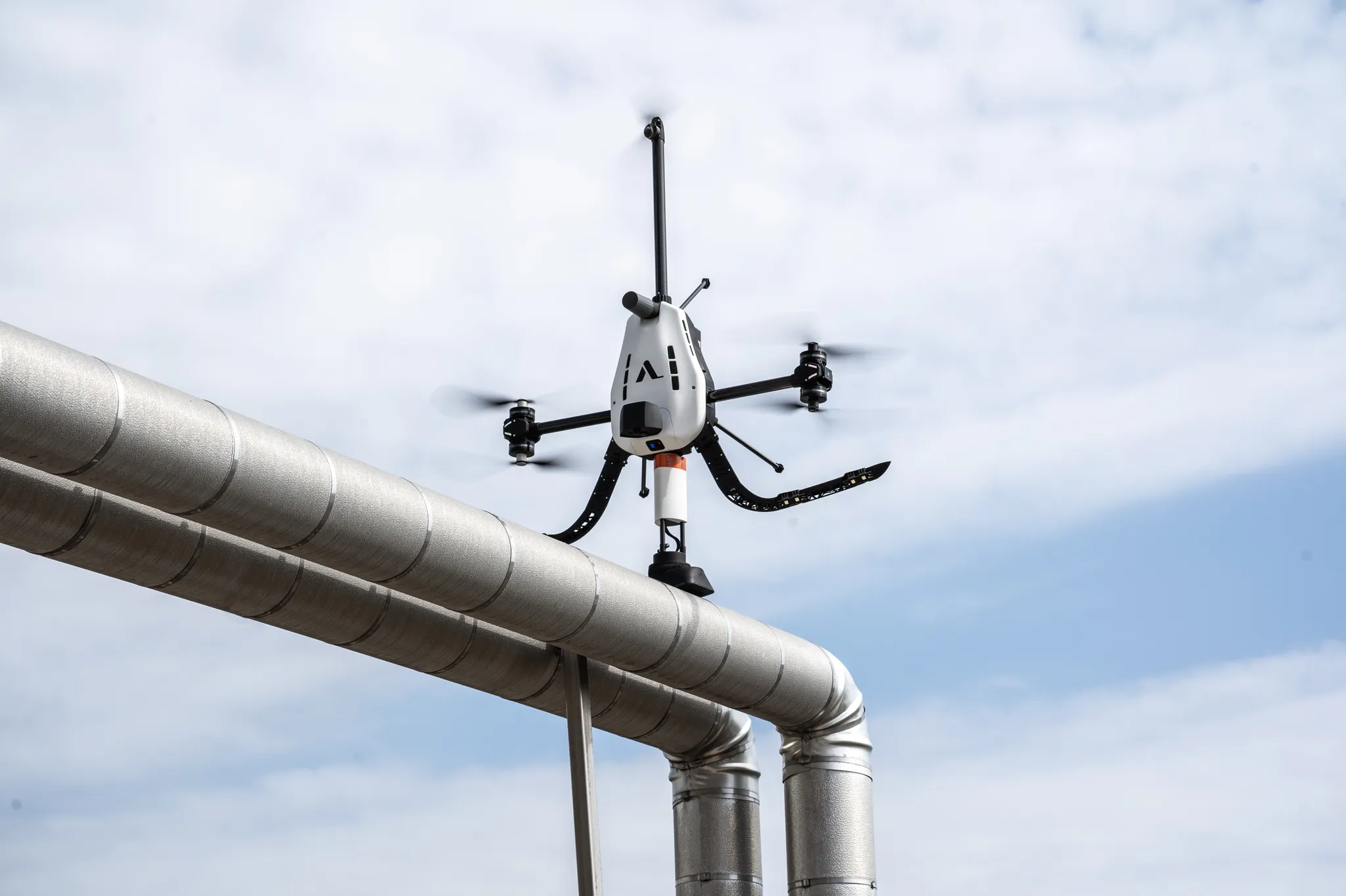 Inspection drone hovering next to industrial pipework for contact-based NDT measurement