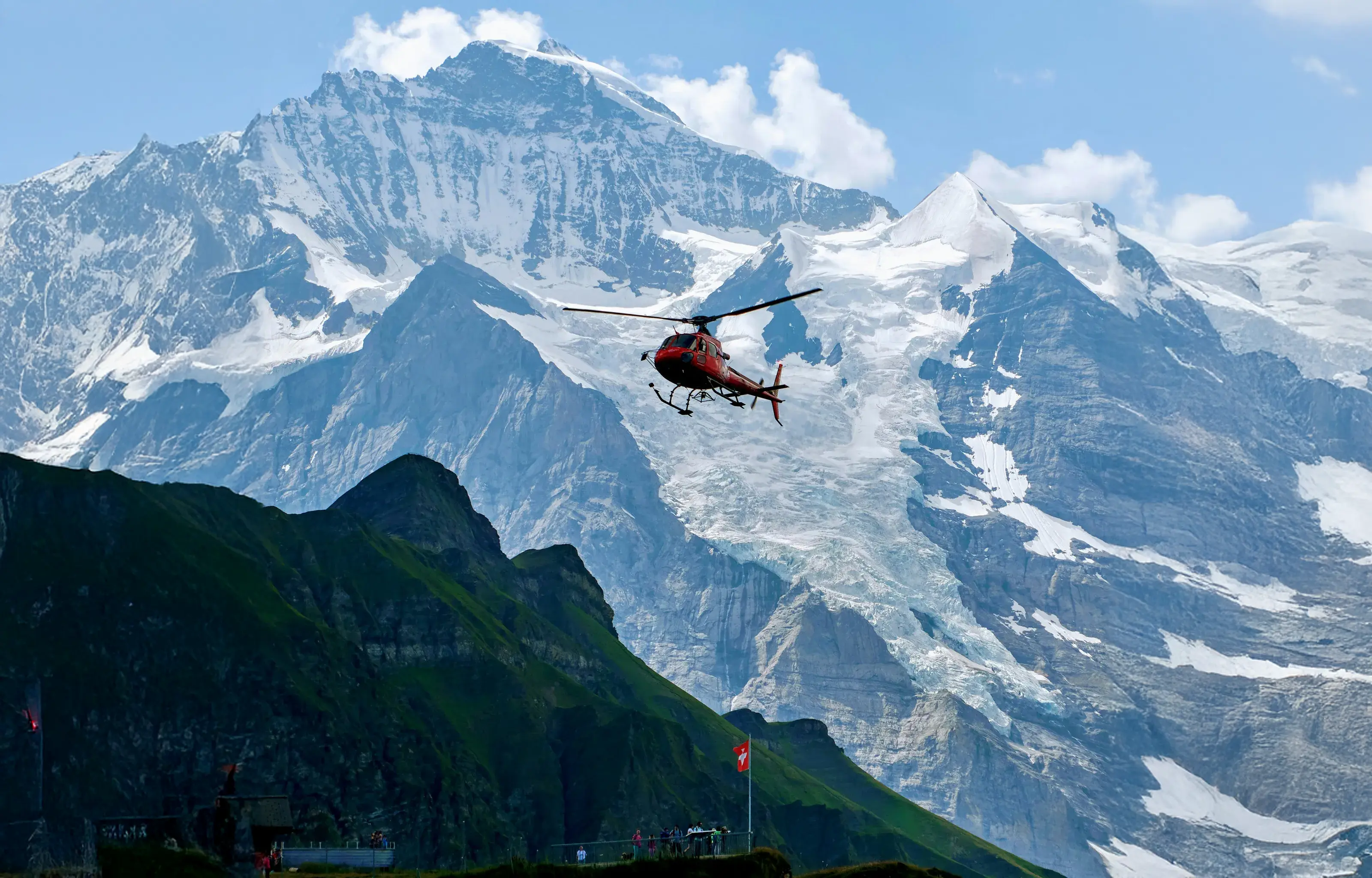 Red survey helicopter flying past snow-capped Alpine peaks during a LiDAR mapping mission