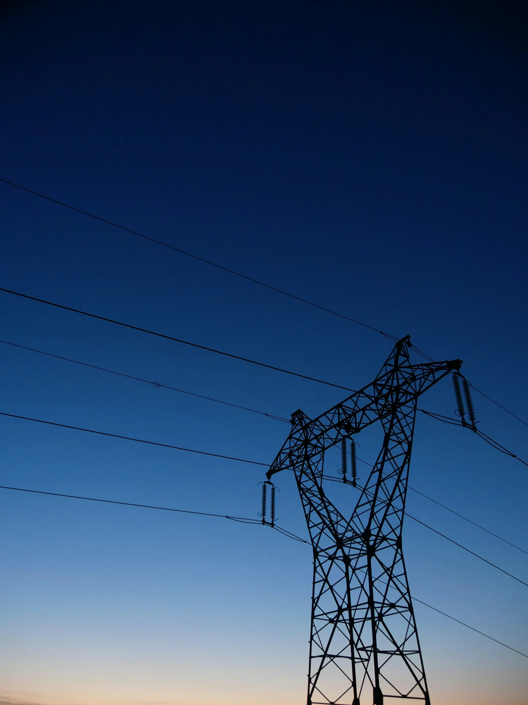 Silhouette of a high-voltage transmission tower and power lines at dusk