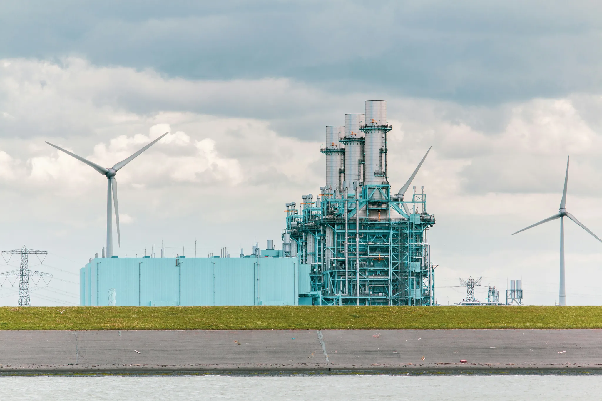 Power generation plant with cooling towers and wind turbines in the background