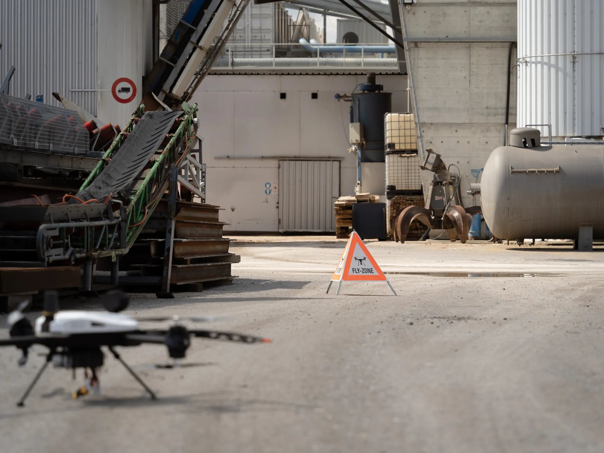 Inspection drone taking off at an industrial site with warning signage and equipment