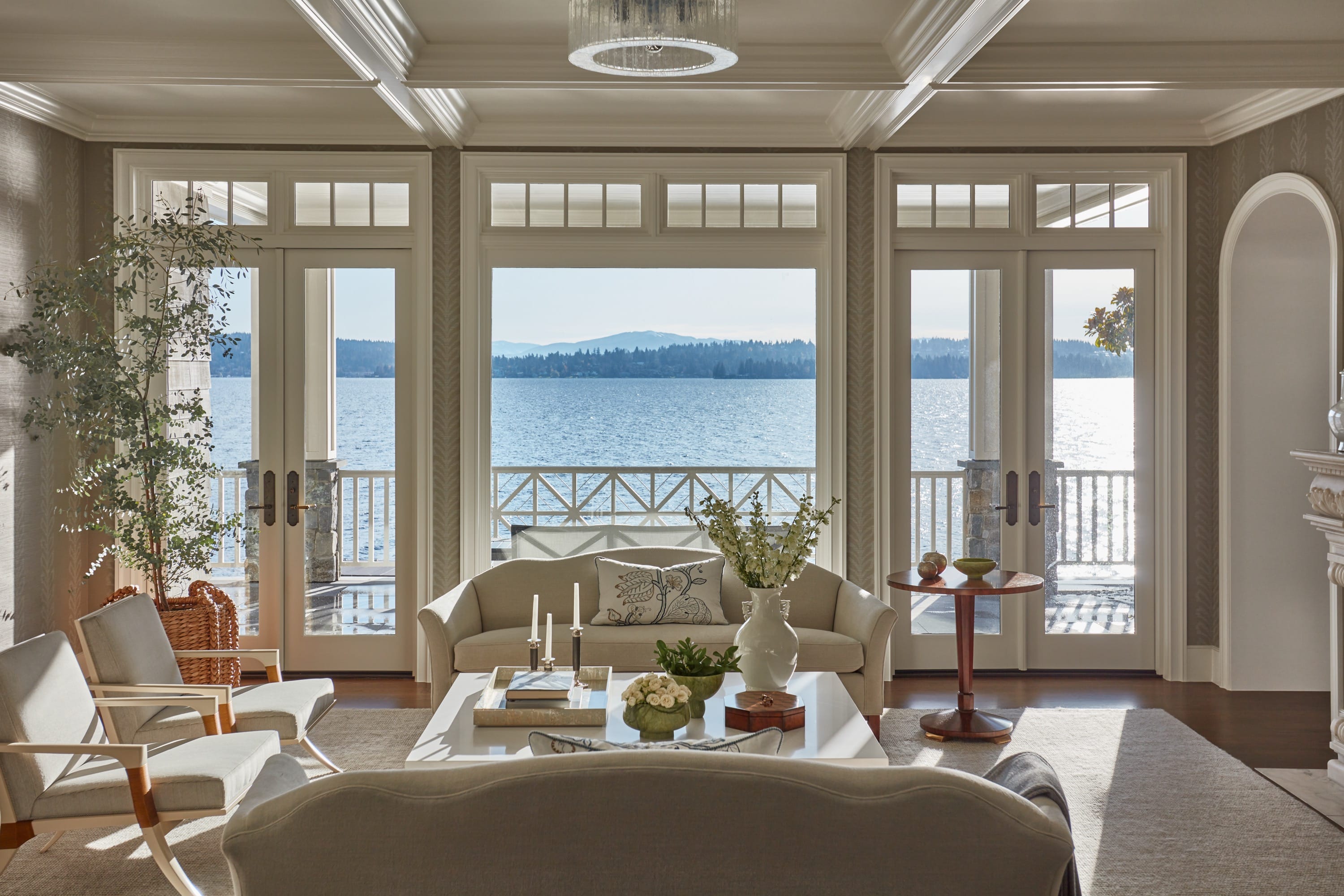 Elegant living room with neutral seating, large windows and doors, opening to a balcony with expansive water views.