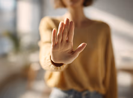 A person wearing a yellow sweater holding up their hand in a stop gesture with a blurred background.