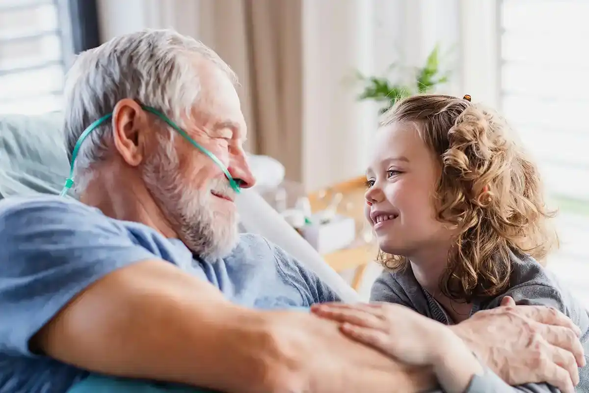 Oudere man met zuurstofslang kijkt liefdevol naar kleinkind. Uitgebreide gids over leven met COPD en de zorg die daarbij komt kijken.