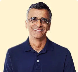 Man with short gray hair and glasses smiling, wearing a navy blue polo shirt on light background.