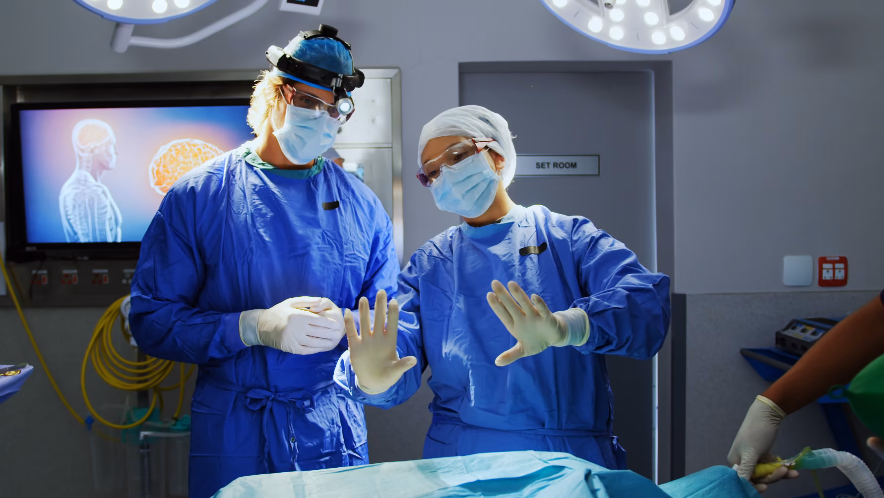 Field Clinical Specialist in blue scrubs, masks, and gloves training site personnel for a trial surgery in an operating room.