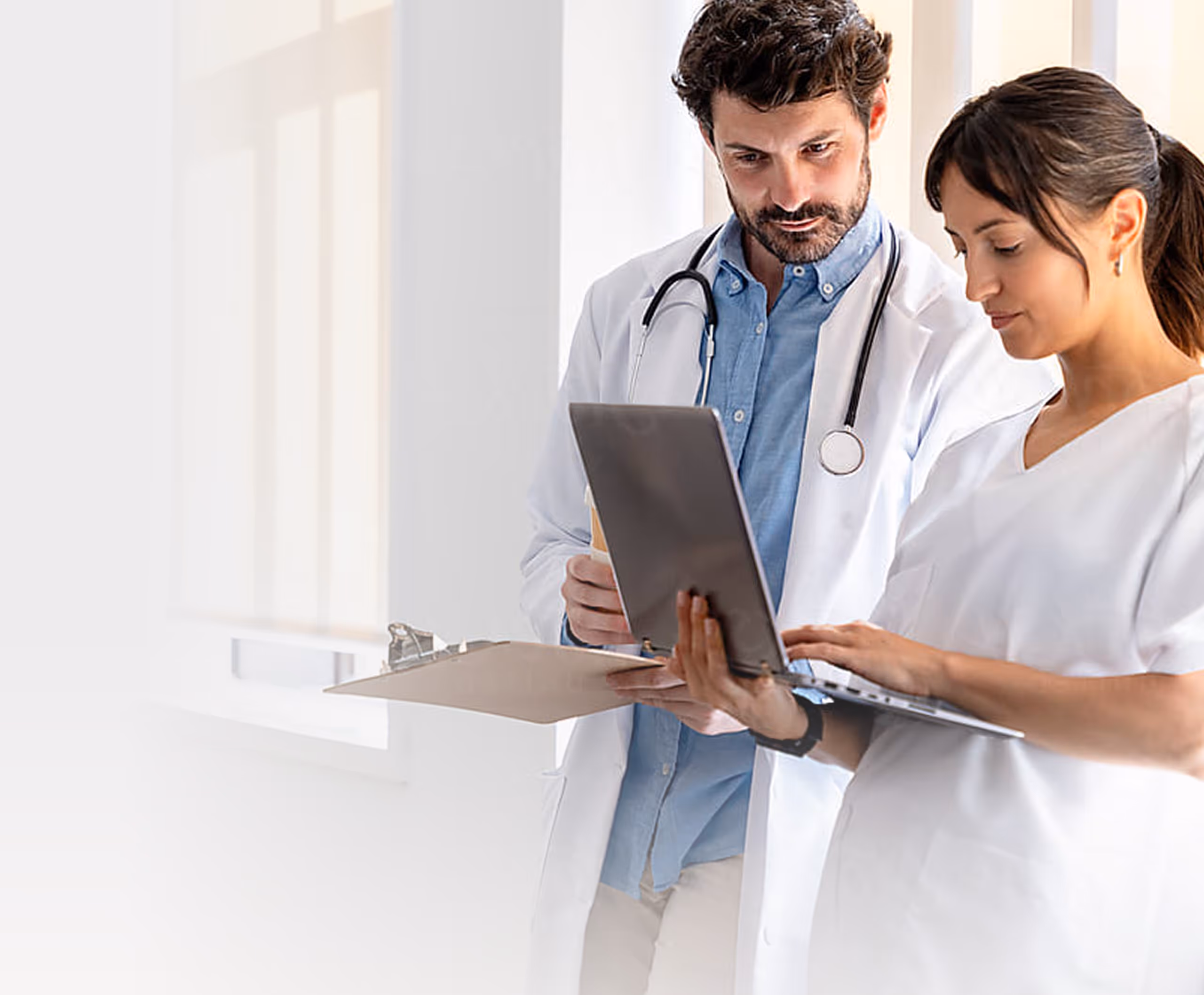 Male doctor and female nurse reviewing information on a laptop in a bright medical office.