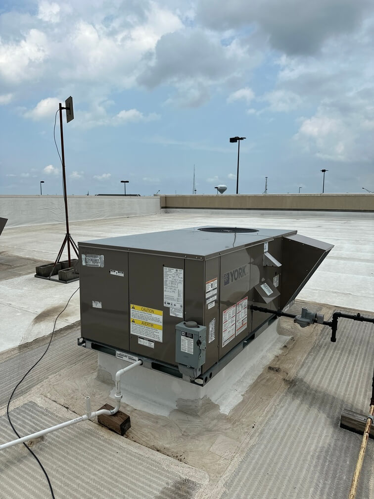 York rooftop HVAC unit installed on a commercial building with pipes and wiring connections under a partly cloudy sky.