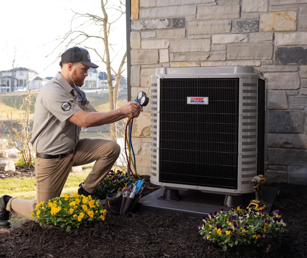 Technician kneeling outside a house while servicing an air conditioning unit with gauges and tools nearby.