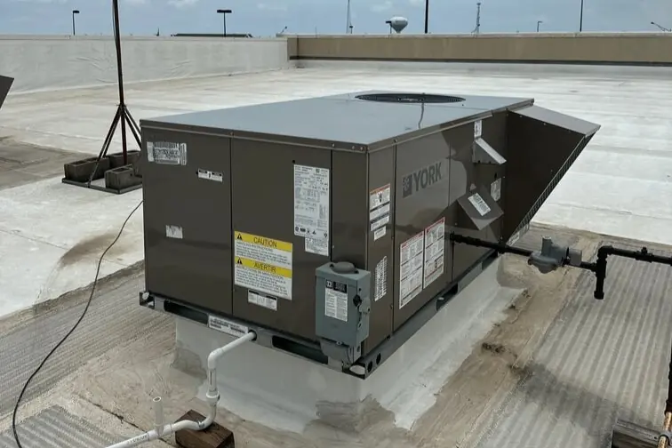 York rooftop HVAC unit installed on a commercial building with pipes and wiring connections under a partly cloudy sky.