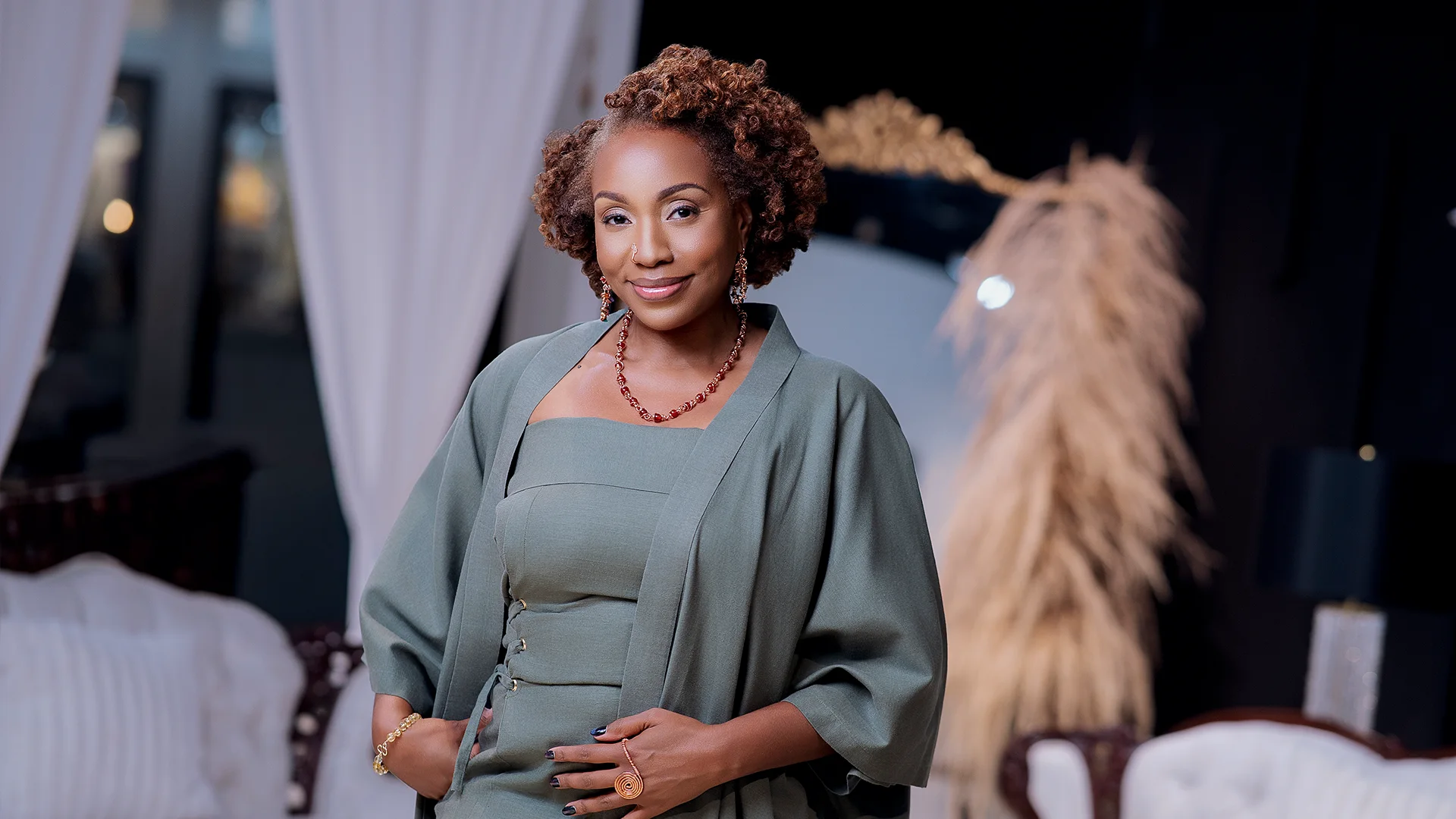 Confident woman with curly hair wearing a green dress and matching jacket, smiling with hands in pockets.