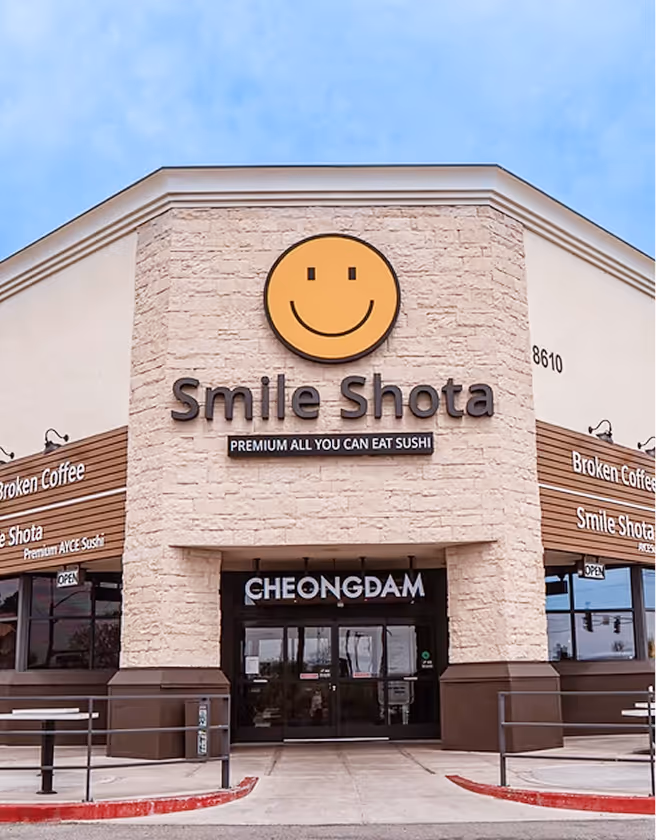 Exterior of Smile Shota restaurant featuring a large smiley face logo and a sign that reads 'Premium All You Can Eat Sushi'.
