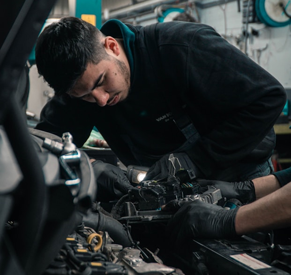 Mechanic in black gloves inspecting and repairing a car engine in a workshop.