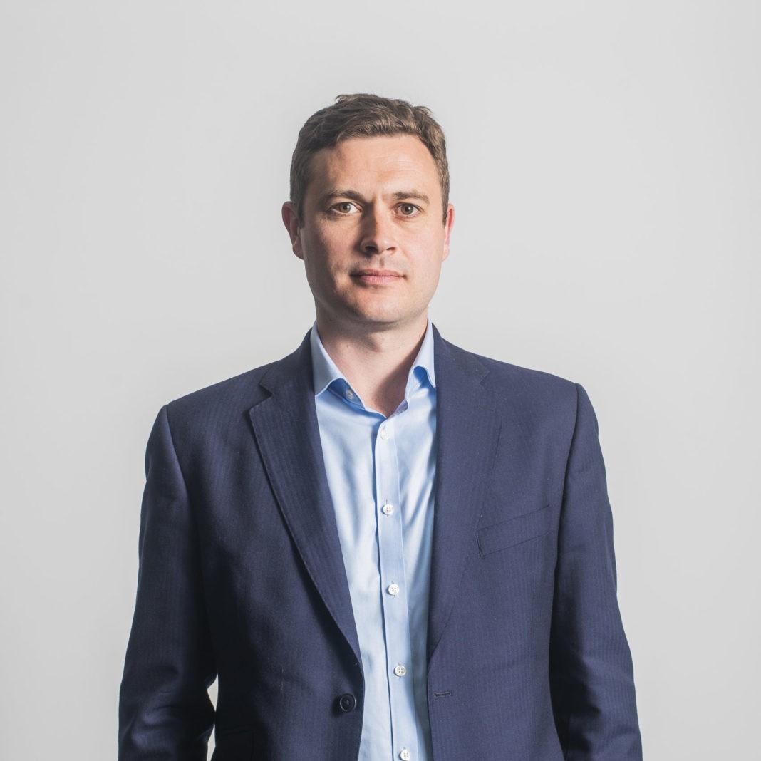 Mechanic in black gloves inspecting and repairing a car engine in a workshop.