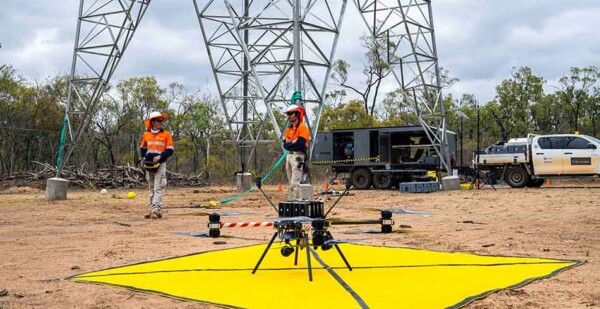 Drone operators stand near drone with transmission tower behind them