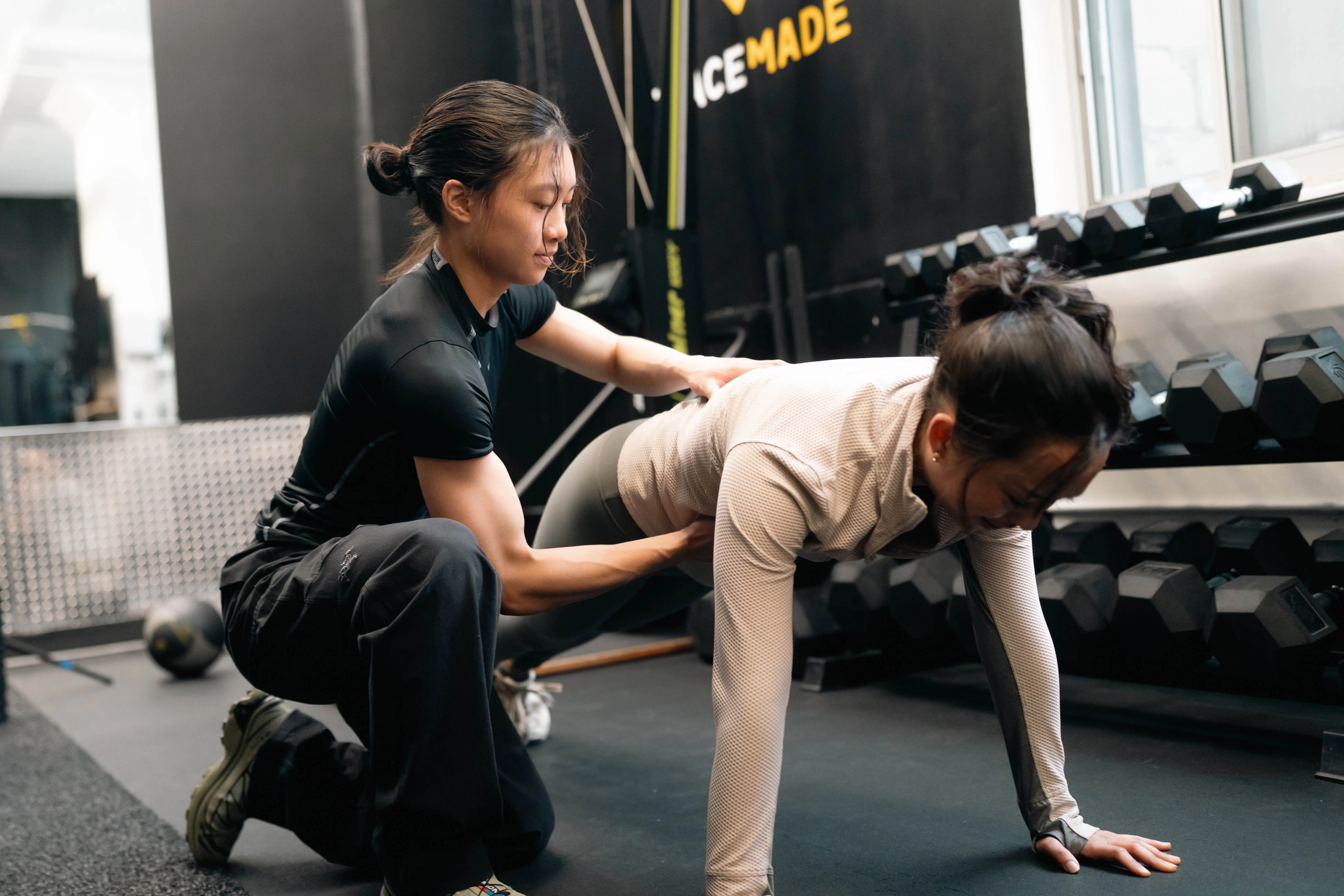 A personal trainer supporting her client in a plank.