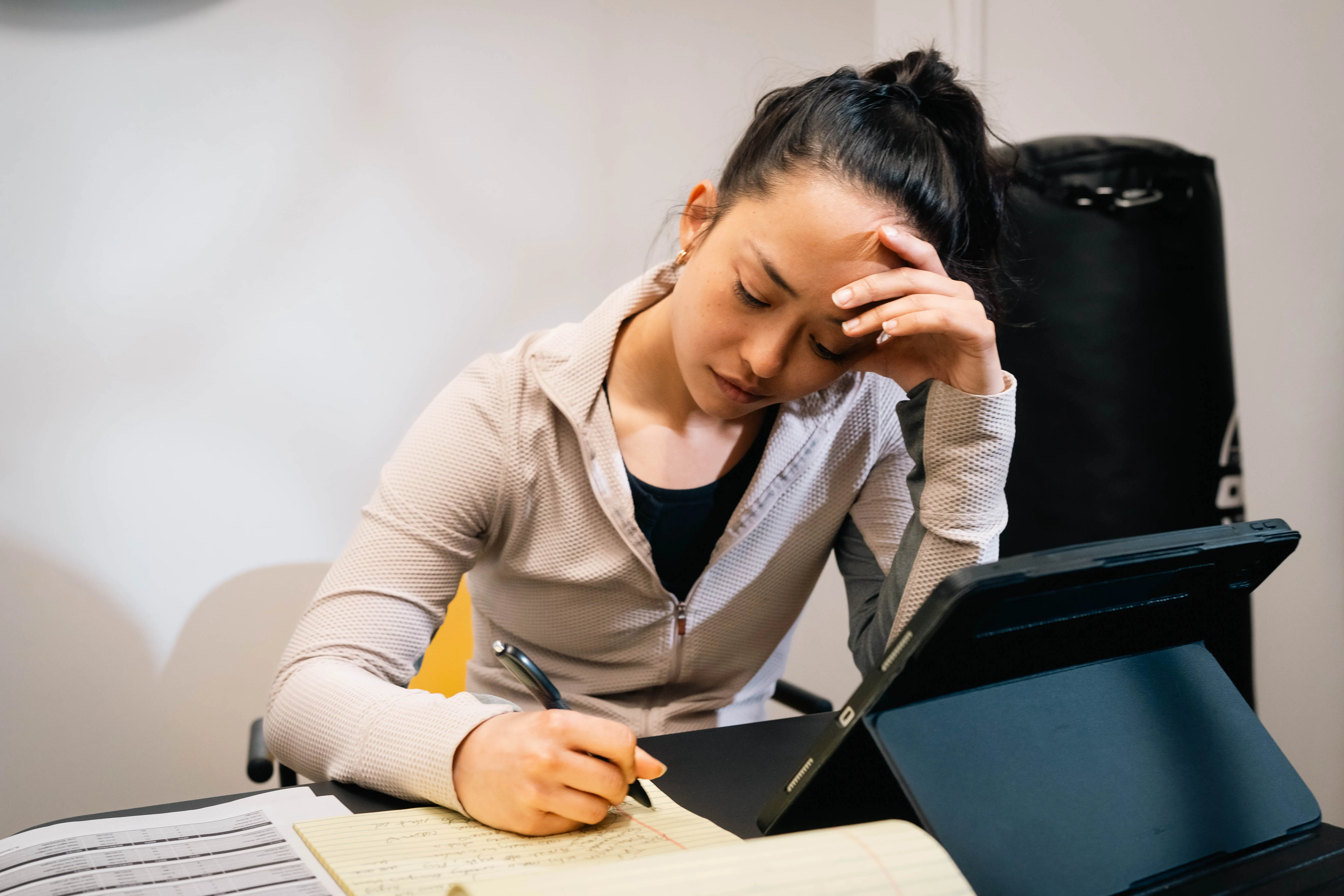 An overwhelmed personal trainer taking notes with multiple devices at a desk.