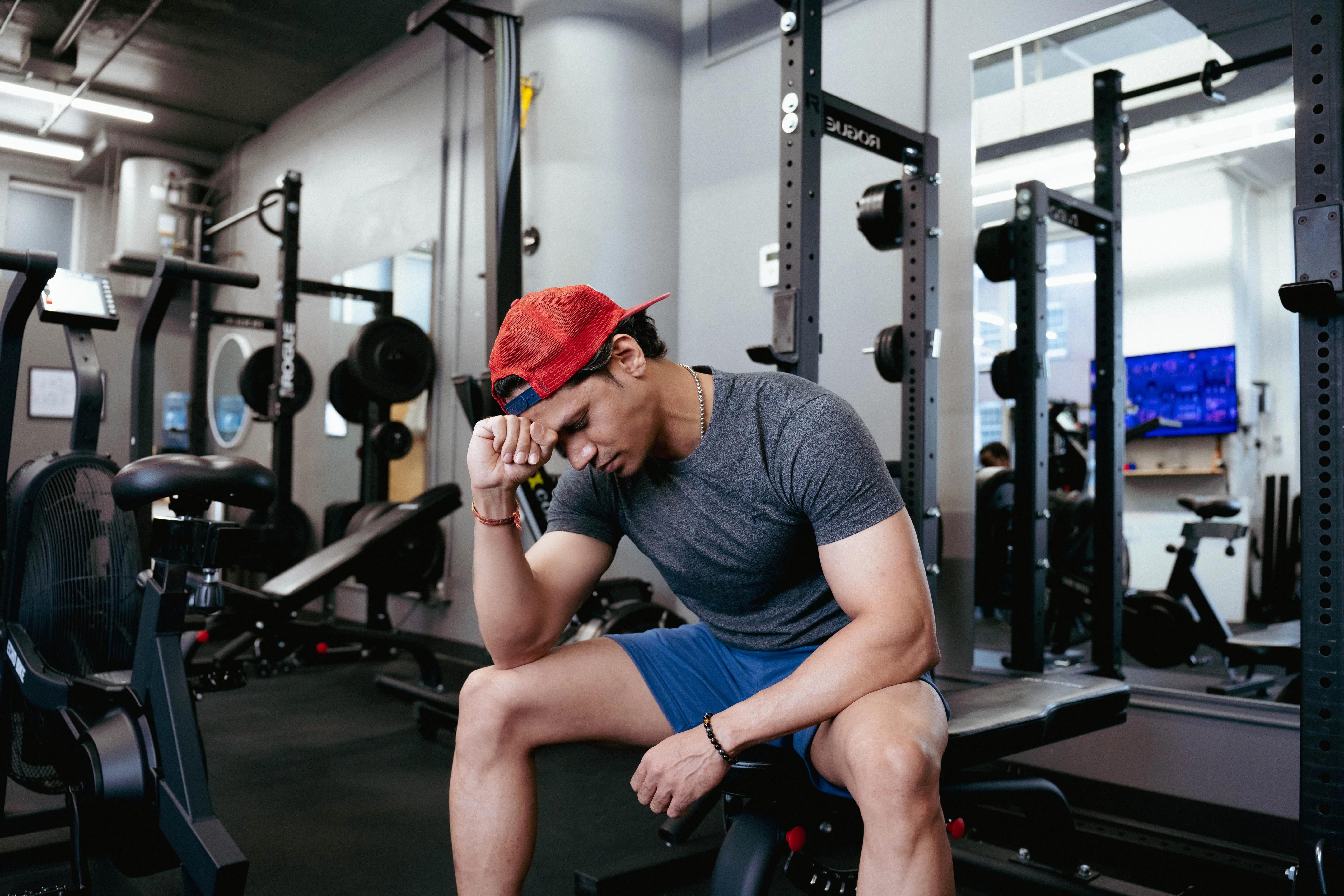 A distressed man leaning on his fist and sitting on exercise equipment.
