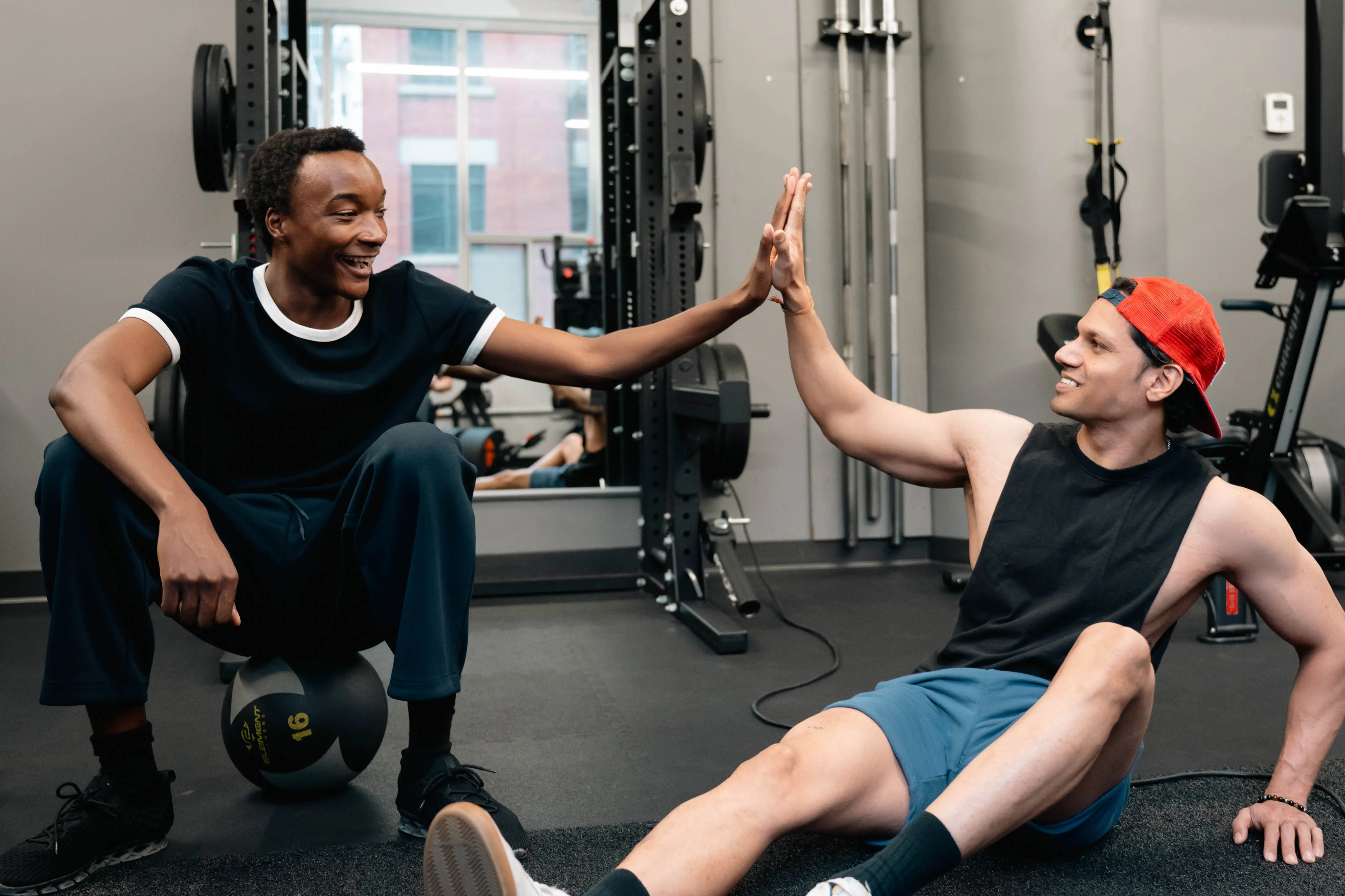 A personal trainer and a client high-fiving on the gym floor.