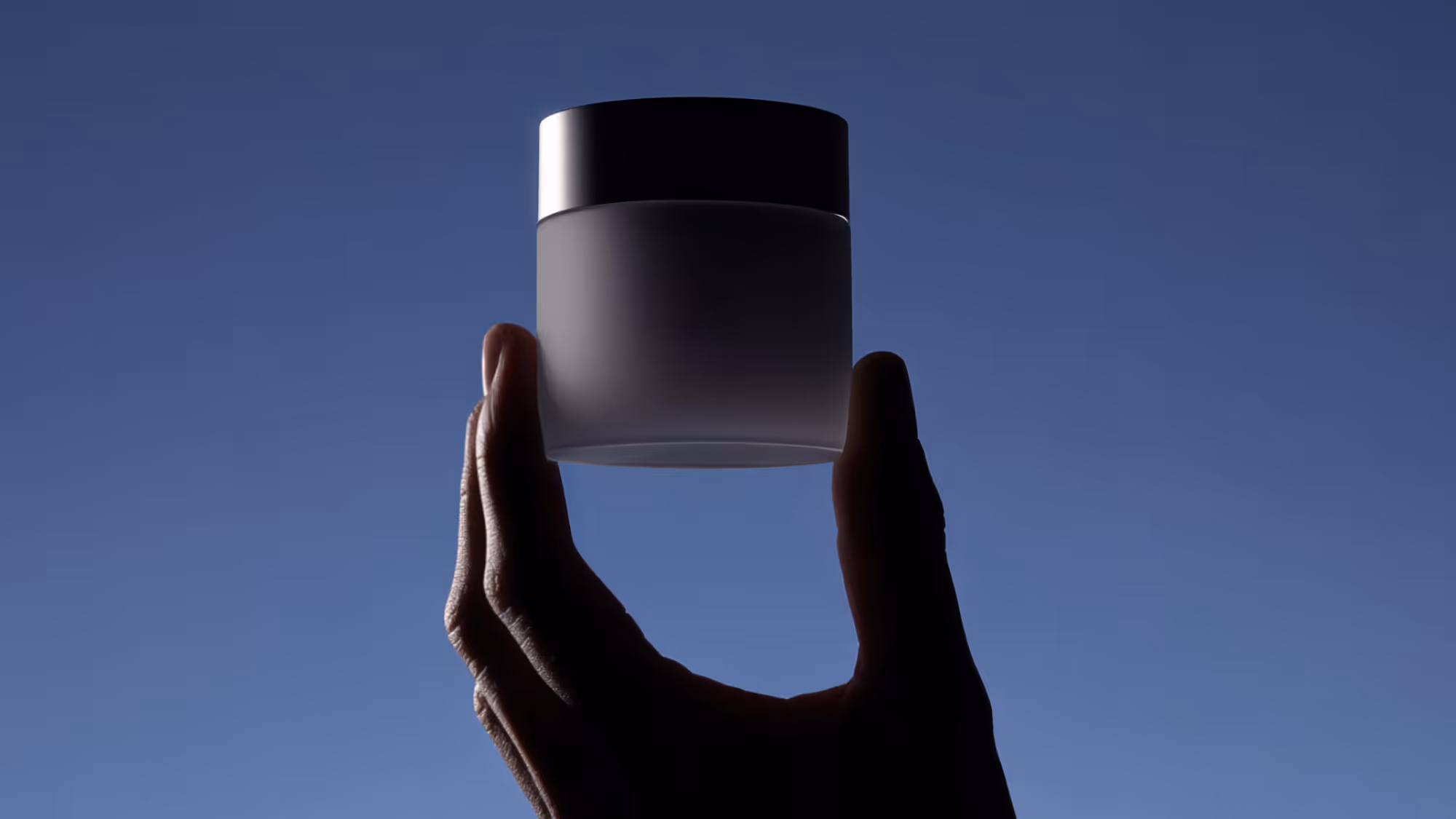 Hand holding a small jar on a blue background.