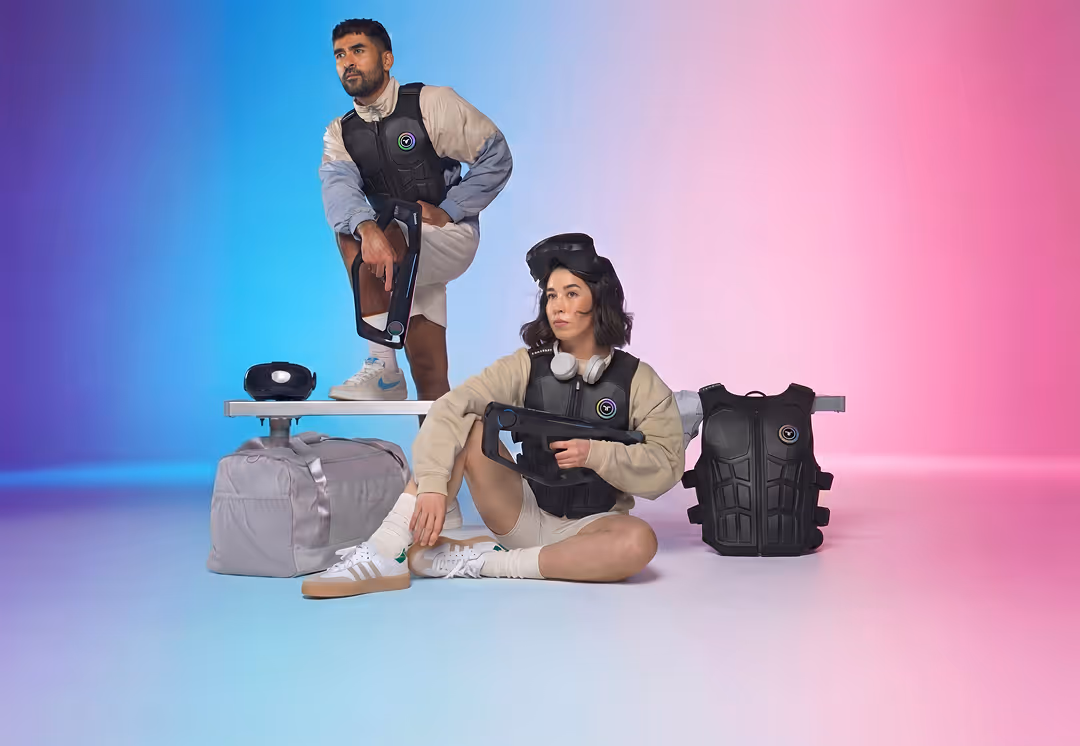 Man and woman wearing black haptic vests, holding futuristic guns, with VR headset and extra vest beside them on a gradient blue and pink background.
