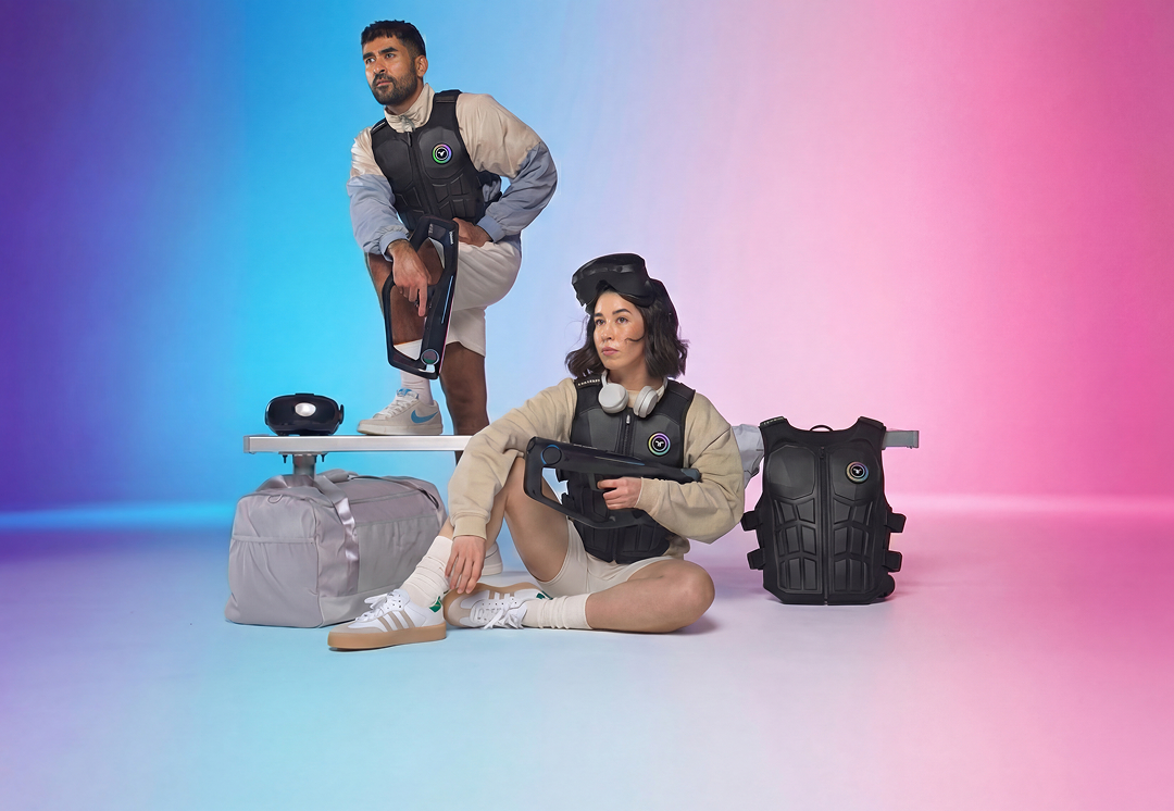 Man and woman wearing black haptic vests, holding futuristic guns, with VR headset and extra vest beside them on a gradient blue and pink background.