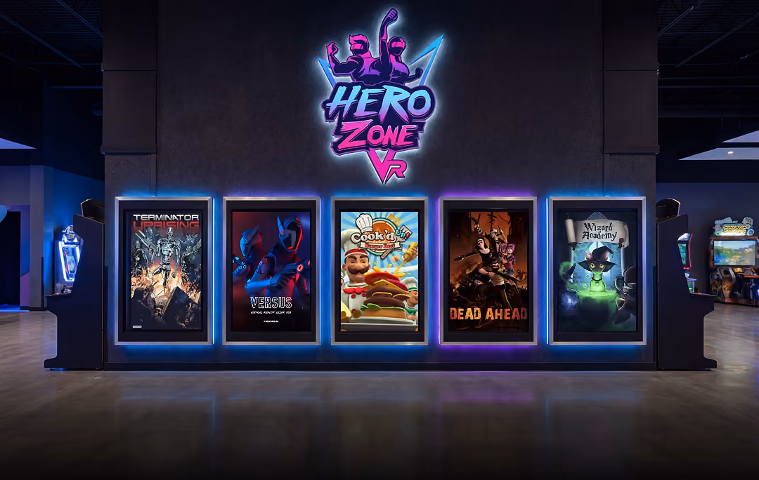Hero Zone VR arcade wall with illuminated posters for games Terminator Uprising, Versus, Cook’d Up, Dead Ahead, and Wizard Academy.