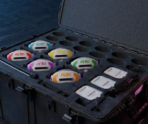 Open black carrying case with six colorful HERO devices and four white rectangular adapters inside.