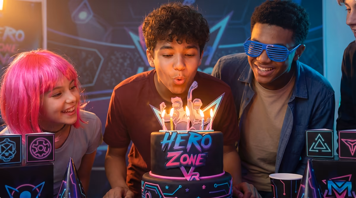 Boy blowing out candles on a two-tiered birthday cake with friends smiling nearby.
