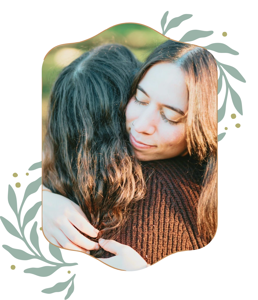 Two people sharing a warm embrace outdoors, one with eyes closed and a gentle smile.
