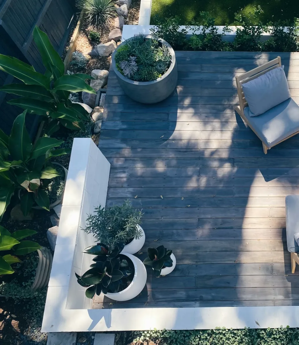 Aerial view of a modern outdoor deck with wood flooring, potted plants, and a cushioned wooden chair.