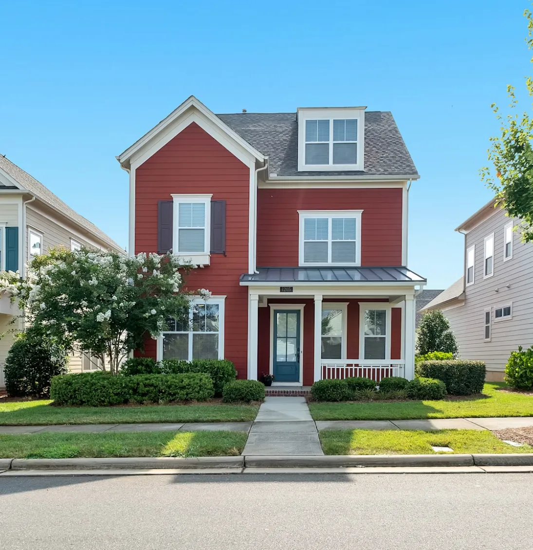 Two-story red house with white trim, a blue front door, and neatly trimmed bushes along the front yard.