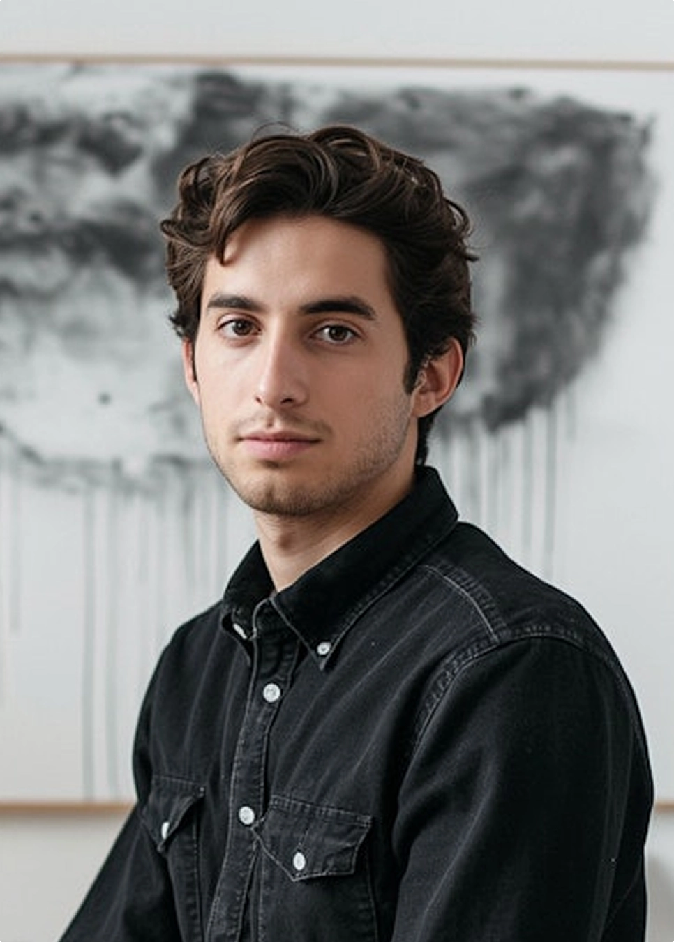 A black and white photo of a man wearing a denim shirt, looking thoughtfully off to the side.