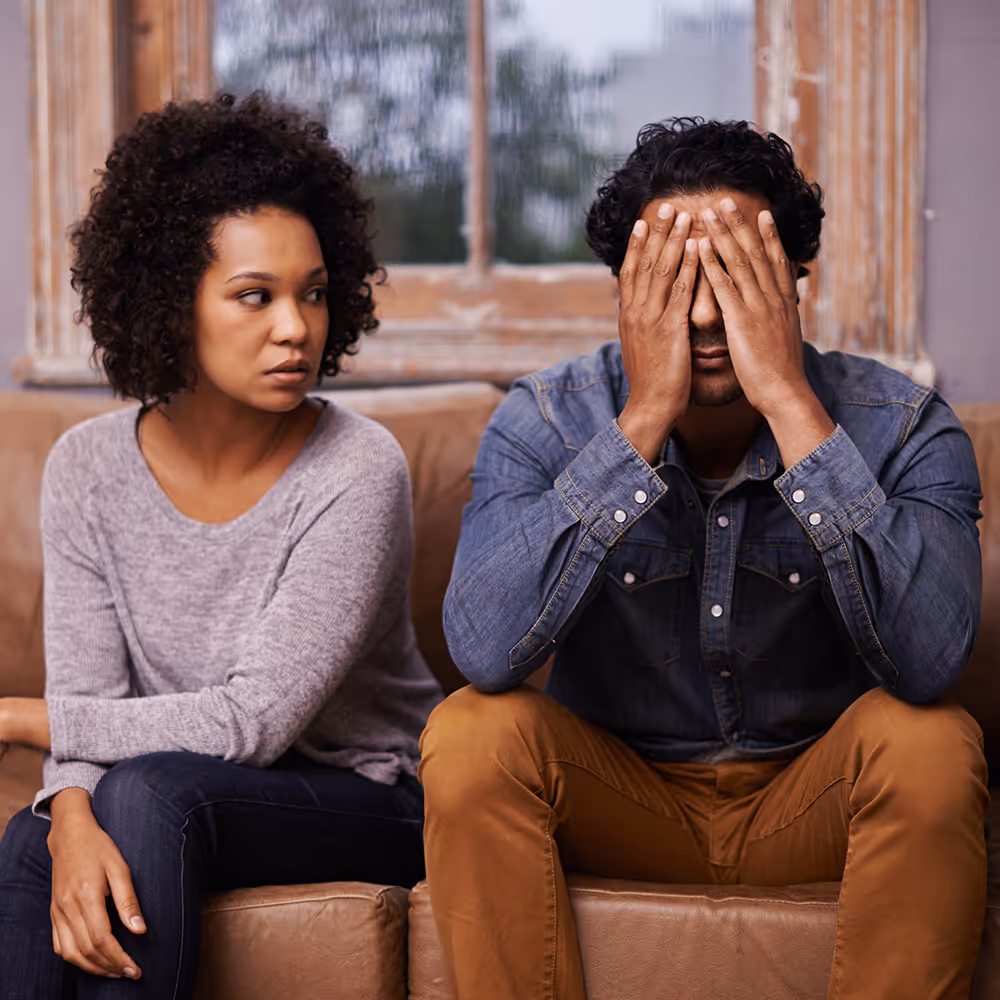 A distressed couple sitting on a couch, illustrating the emotional impact of infidelity and trust ruptures addressed through betrayal and heartbreak counseling at Willow & Stone Counseling in DFW.