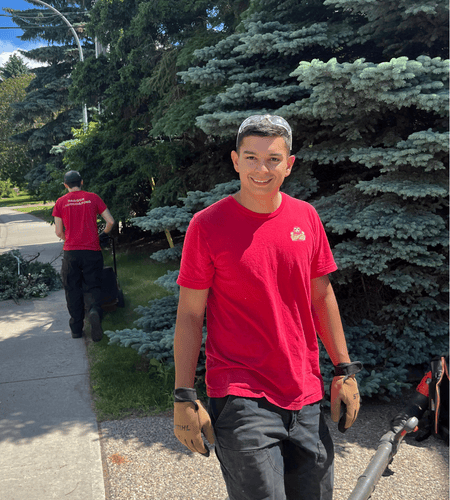An image of Teiran, the owner of Badger Landscaping, smiling on the jobsite while trimming trees in Edmonton, AB.