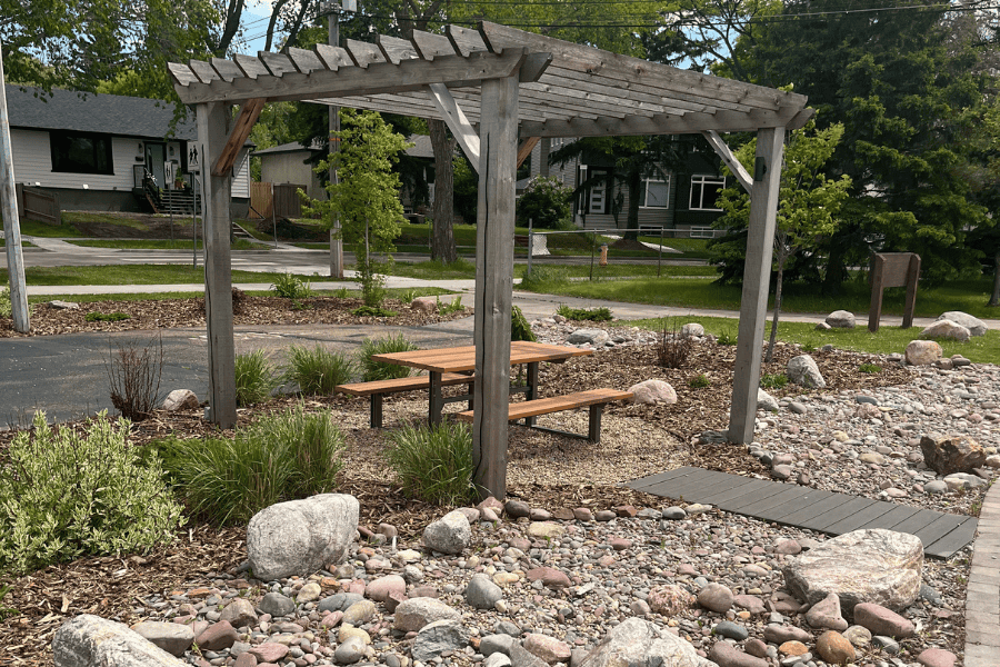 An image of a park in Edmonton with a wooden structure covering a bench. The image showcases a recently completed landscape installation in Edmonton by Badger Landscaping.