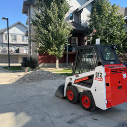 A new Bobcat skid-steer driving towards a pile of beach rocks during an Edmonton landscape install job.