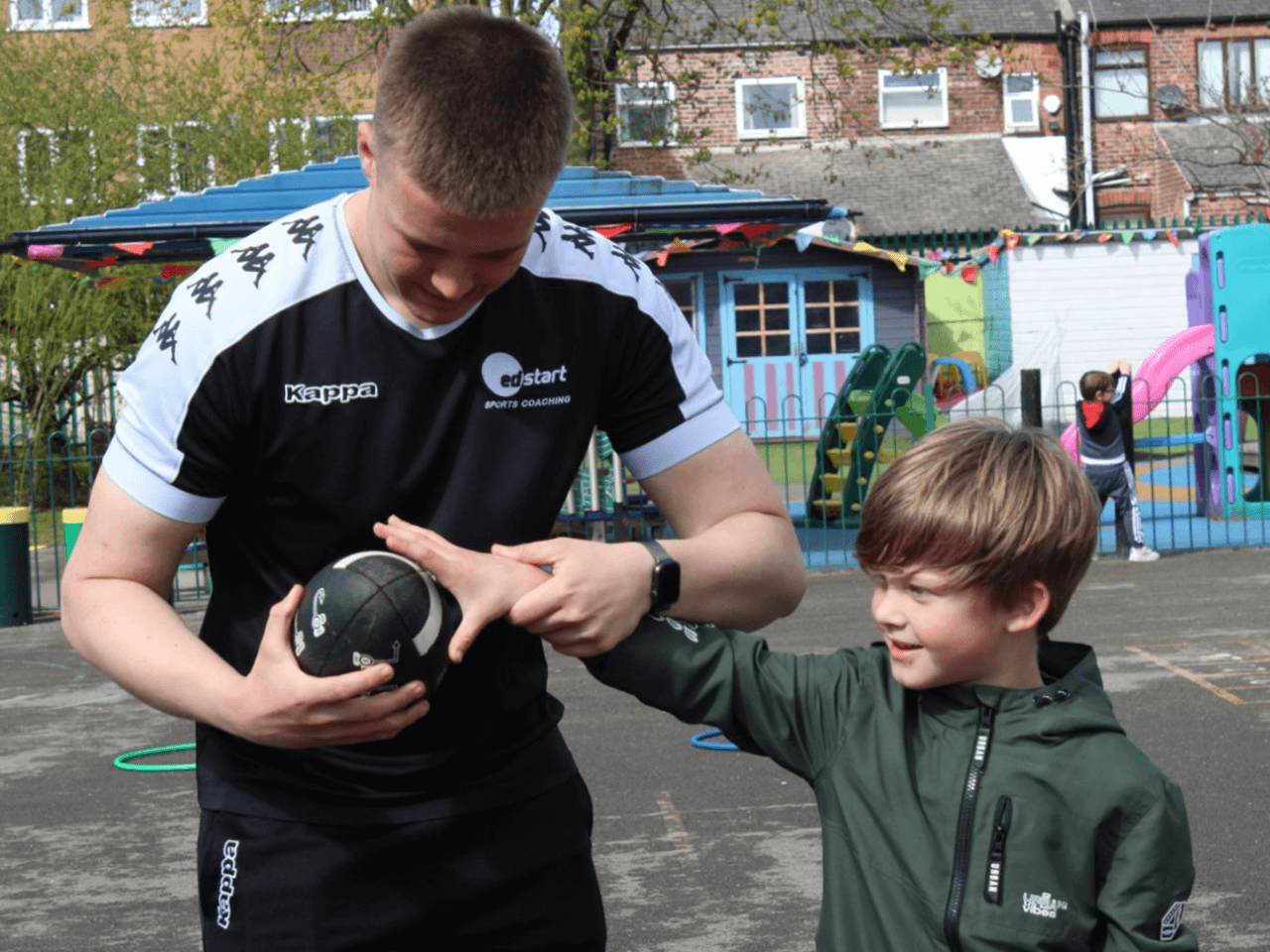 A coach teaching a boy how to hold an American football.