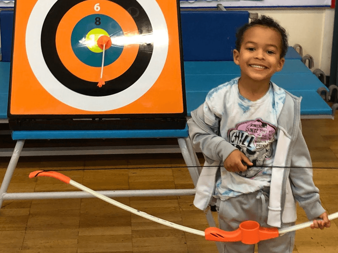 Child smiling holding a bow after getting a bullseye in indoor archery.