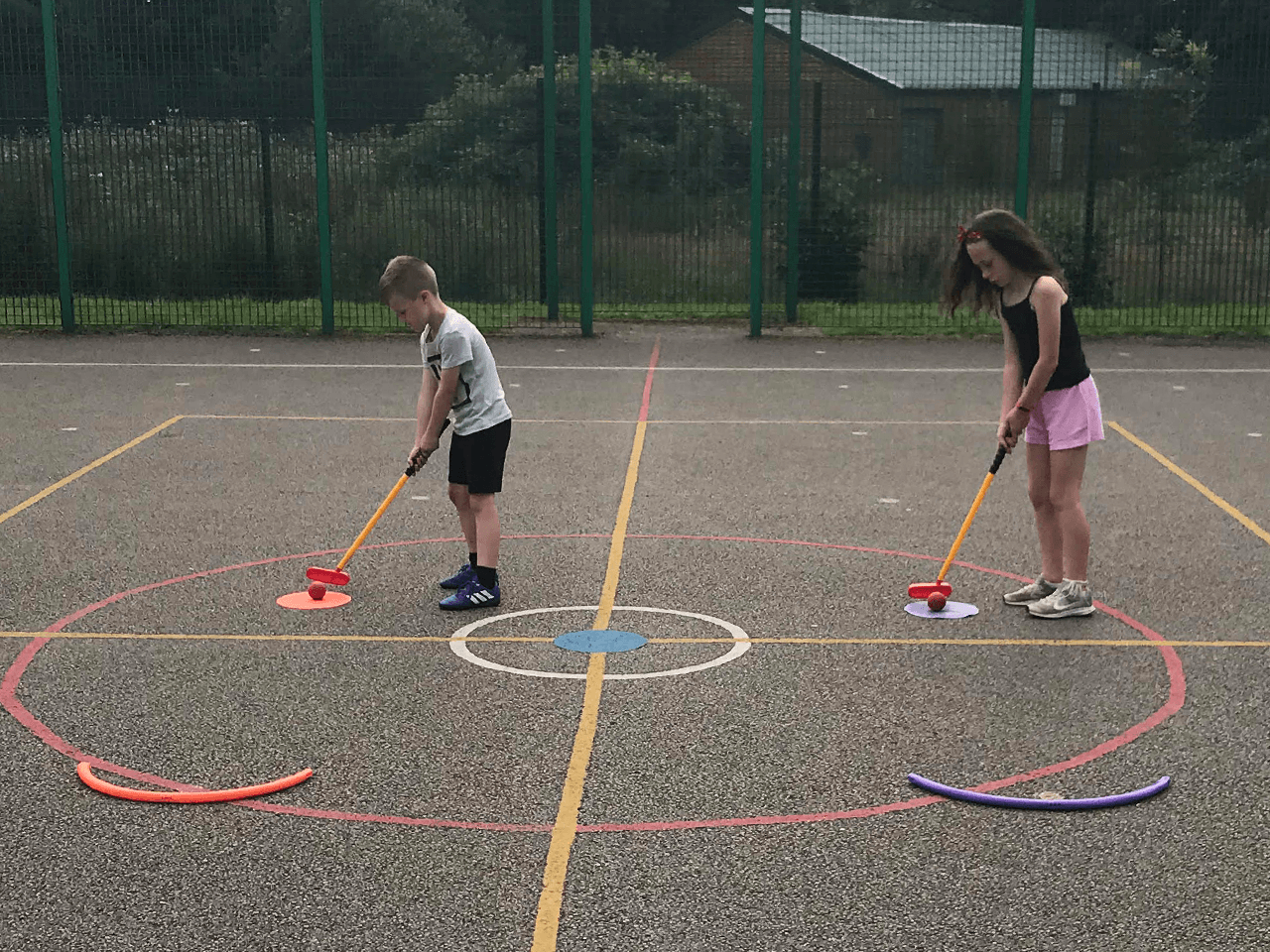 Boy and a girl practicing their golf putting in the playground.