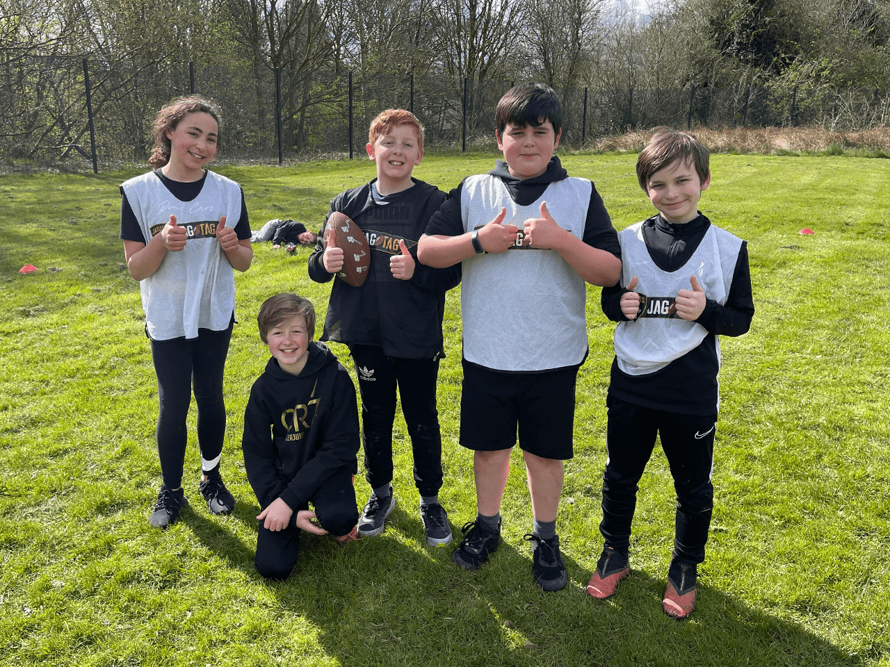 Five children with thumbs up posing for photo wearing JagTag branded vests.