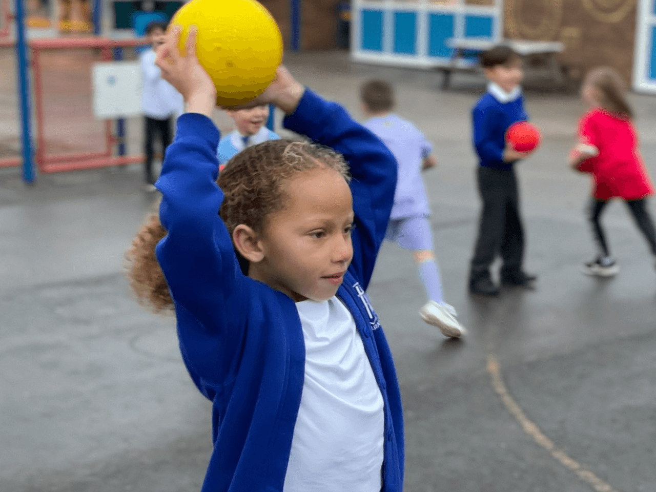 A school girl throwing a ball in the playground.