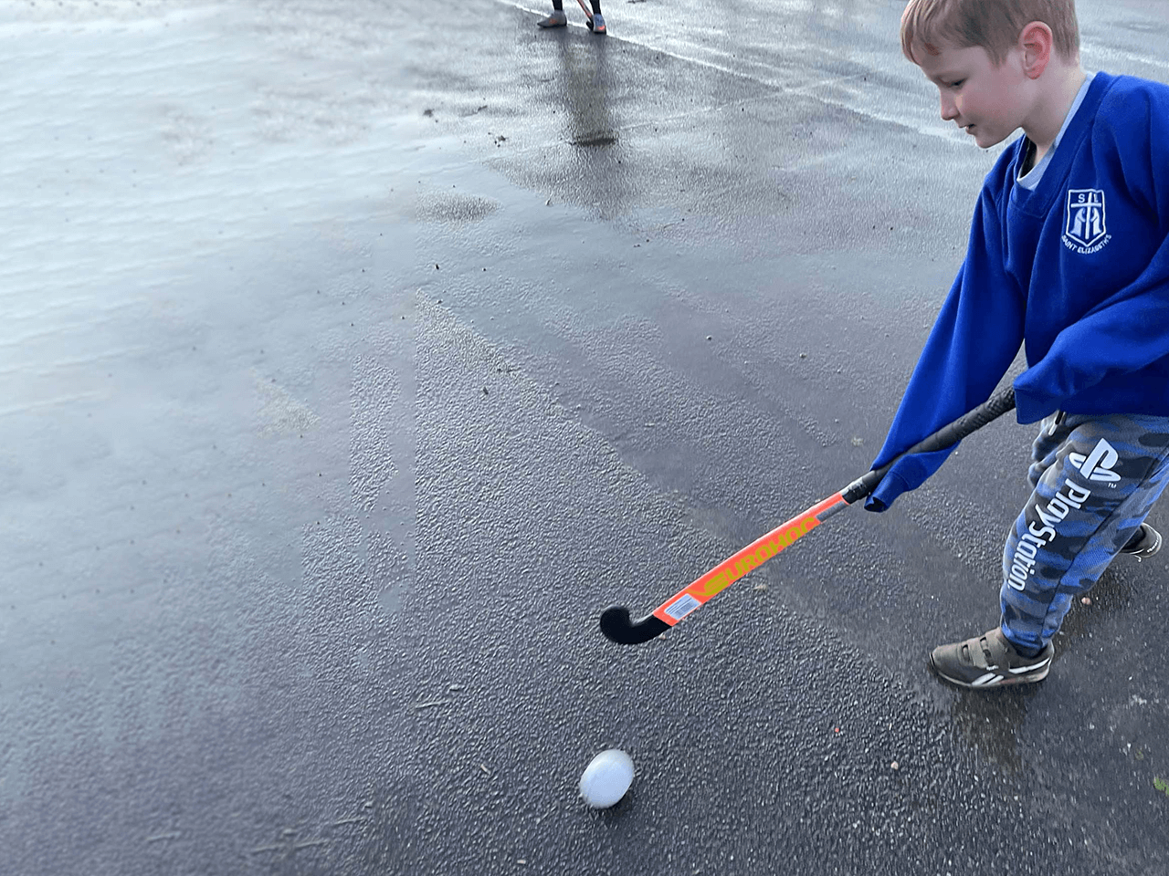 A boy dribbling a ball in hockey.
