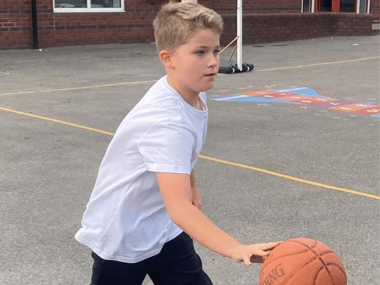 A boy dribbling a basketball in the playground.